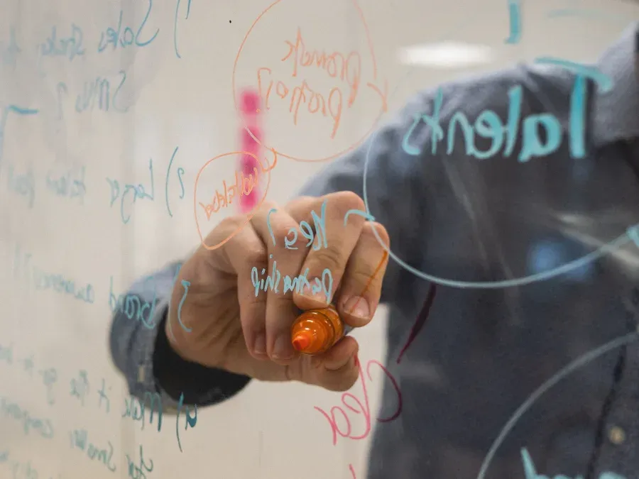 A person mapping growth ideas onto a glass whiteboard in marker