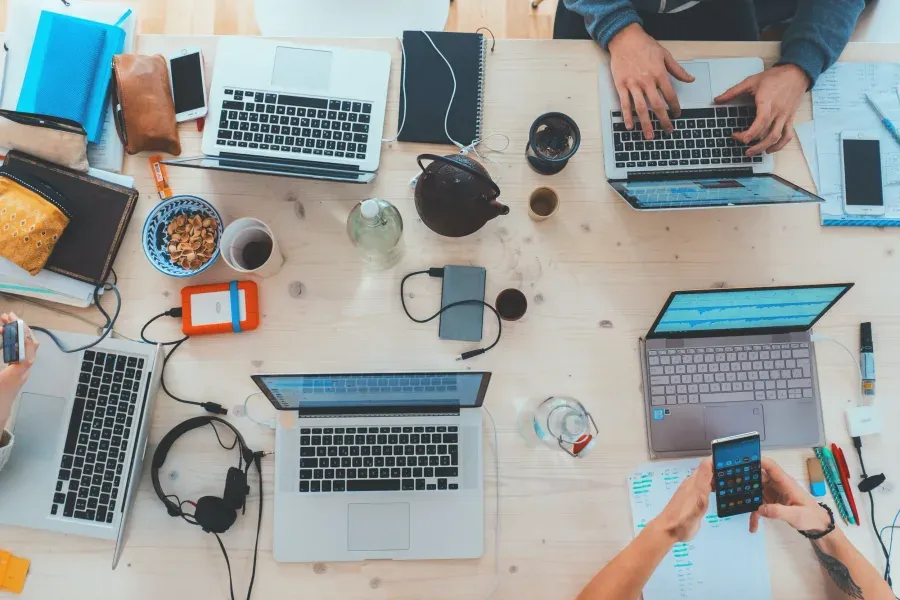 Overhead view of a team working together at a table covered in laptops and devices